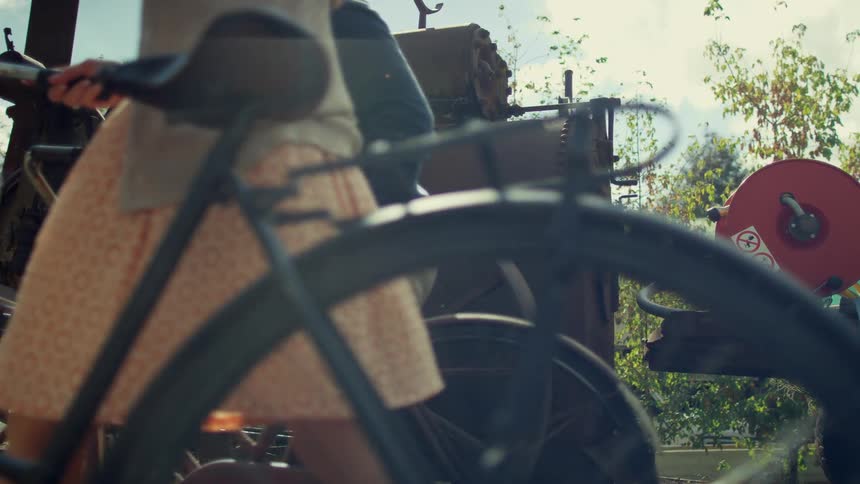 A female wearing a skirt is waking with an old bicycle
