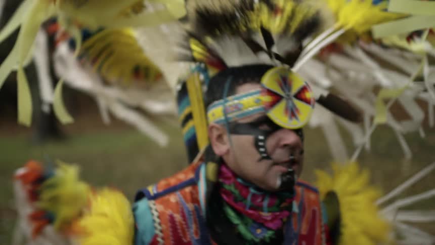 Man dressed in traditional amerindian garb grimaces while dancing traditional dance