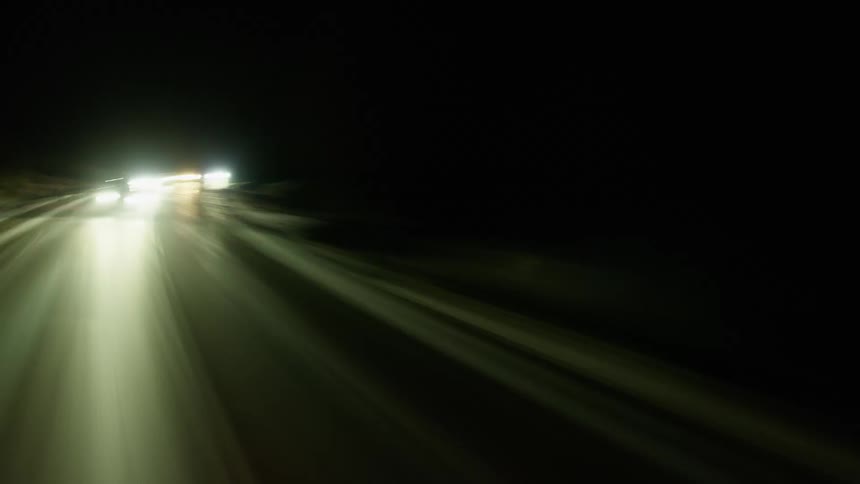 Cars with bright headlights traveling on a road in the dark