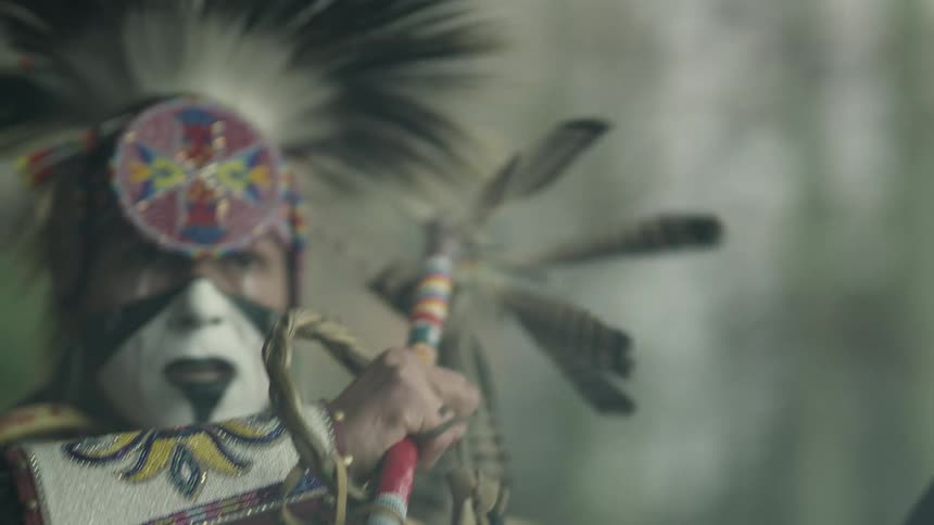 An indigenous man throws his arm forward as he uses a feather whip