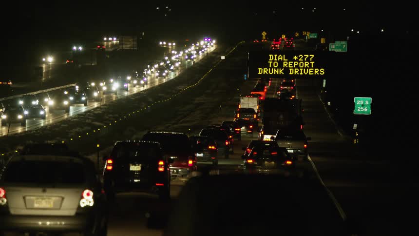 Sign provides public information as heavy traffic moves along divided highway at night
