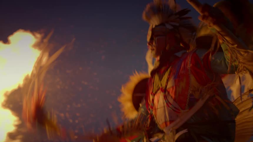 An indigenous man carries a spear as he dances around a fire