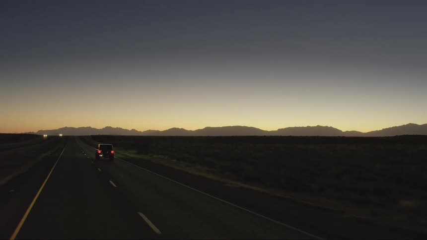 An aerial view of a car traveling on a remote road at dusk