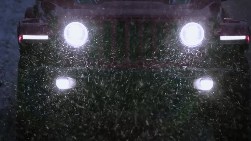 A car with bright headlights driving in a snowstorm at night