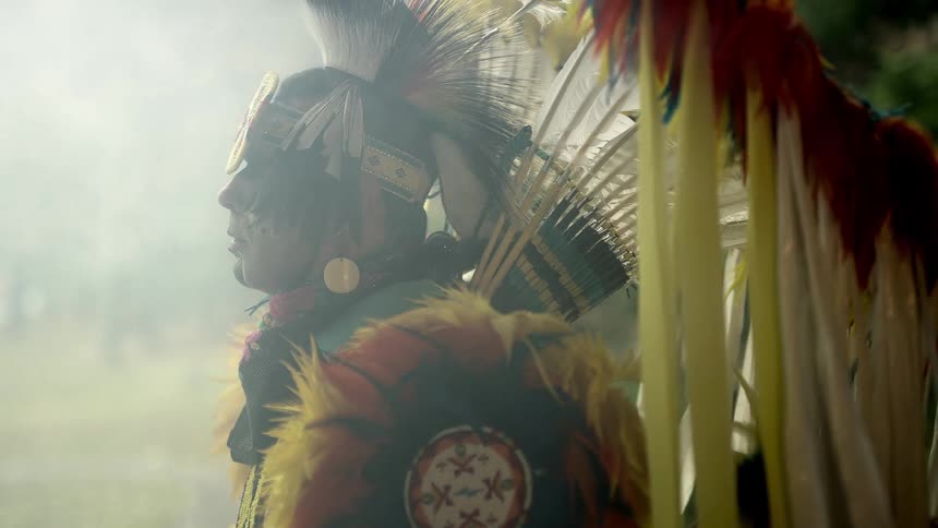 A man with traditional native american clothing with feathers surrounded by smoke