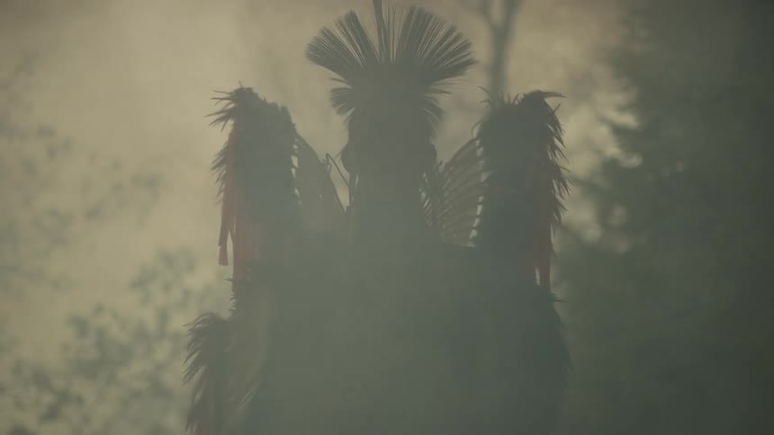 A native american standing outdoors with smoke