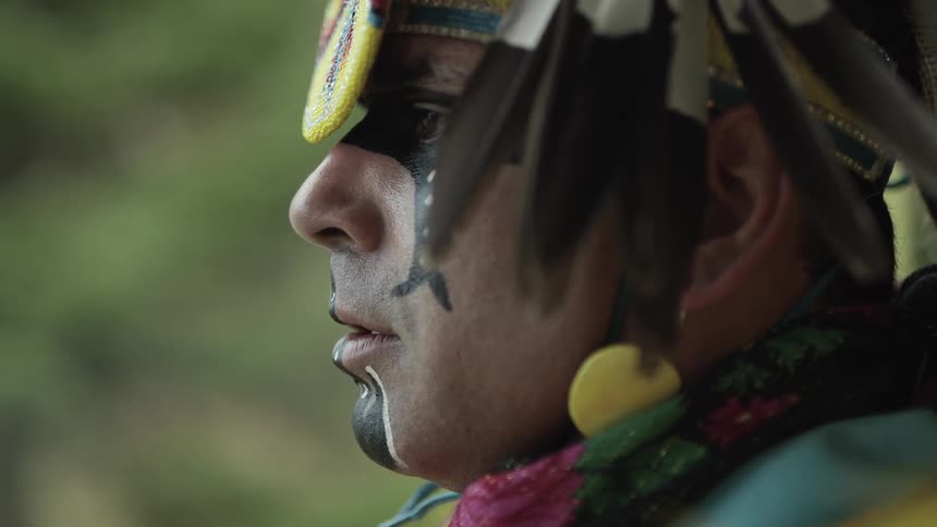 A man in native dress and head wear stands outside
