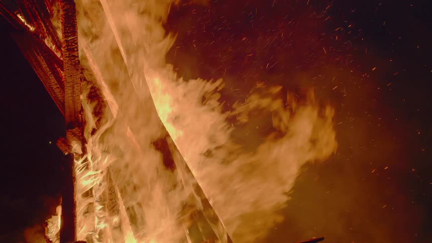 Roaring bonfire sits in middle of burning ground at night releasing smoke and sparks into air