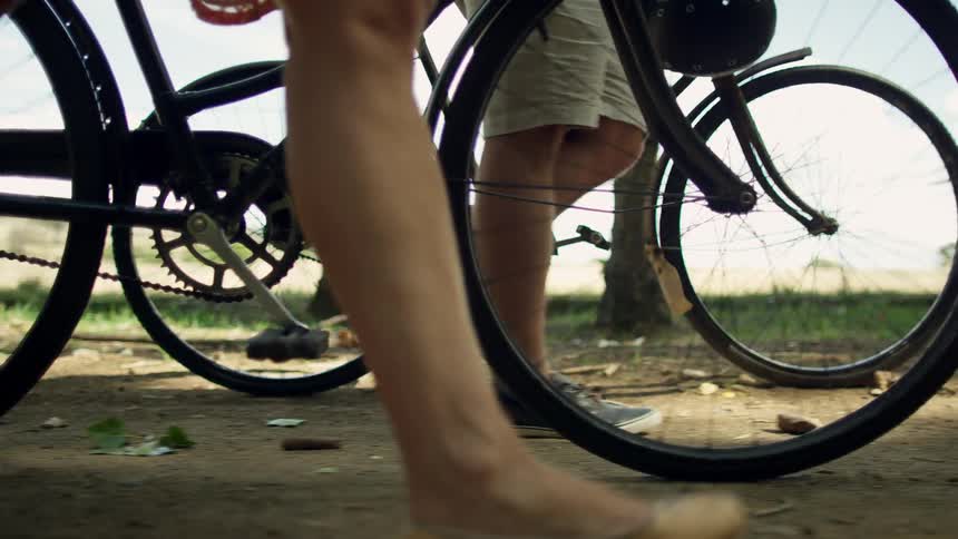 A pair of people push bicycles while walking along a dirt road during the day