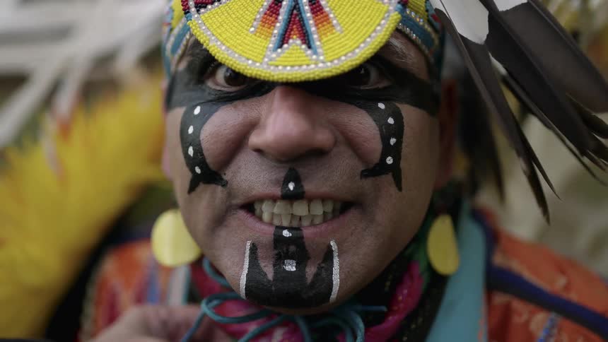 A native american in full costume is dancing and looks forward