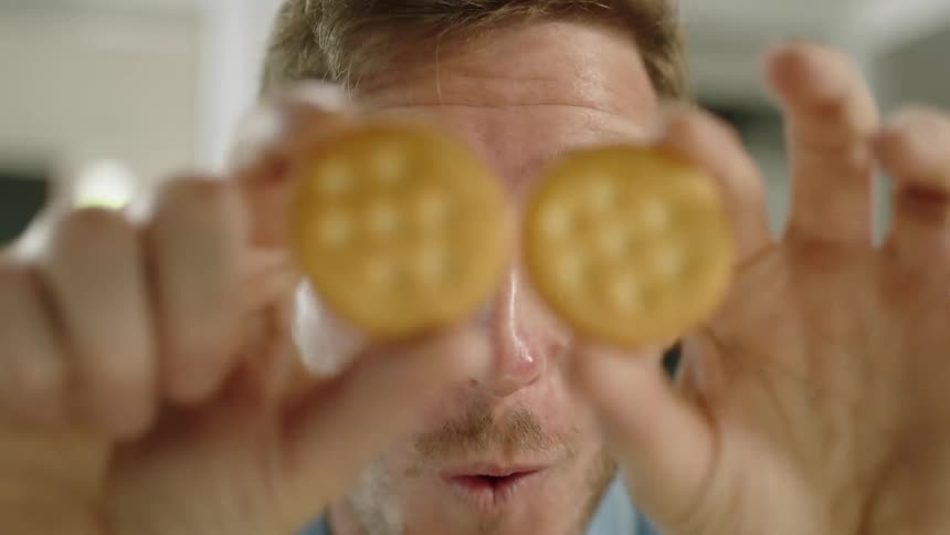 A man playfully covers his eyes with round crackers