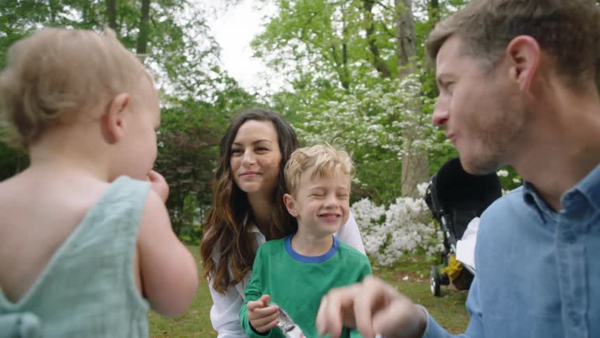 A family of four is outside having a picnic and sharing snacks