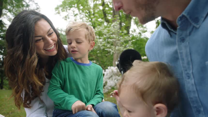 A family is outside together and a child feeds a snack to a younger child