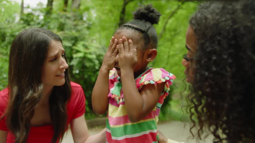 A little girl is playing and covering her eyes and two women are playing the game with the child
