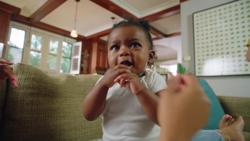 A woman is reclined on a sofa in a home with her daughter sitting on her lap crying until she is given something to eat