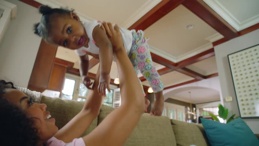 A mom smiles as she raises her daughter up above her