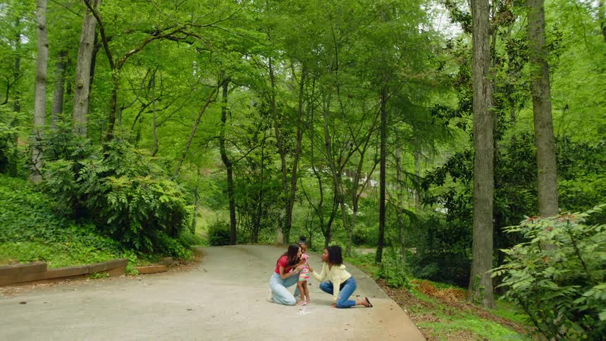 Two women hug young girl in the park