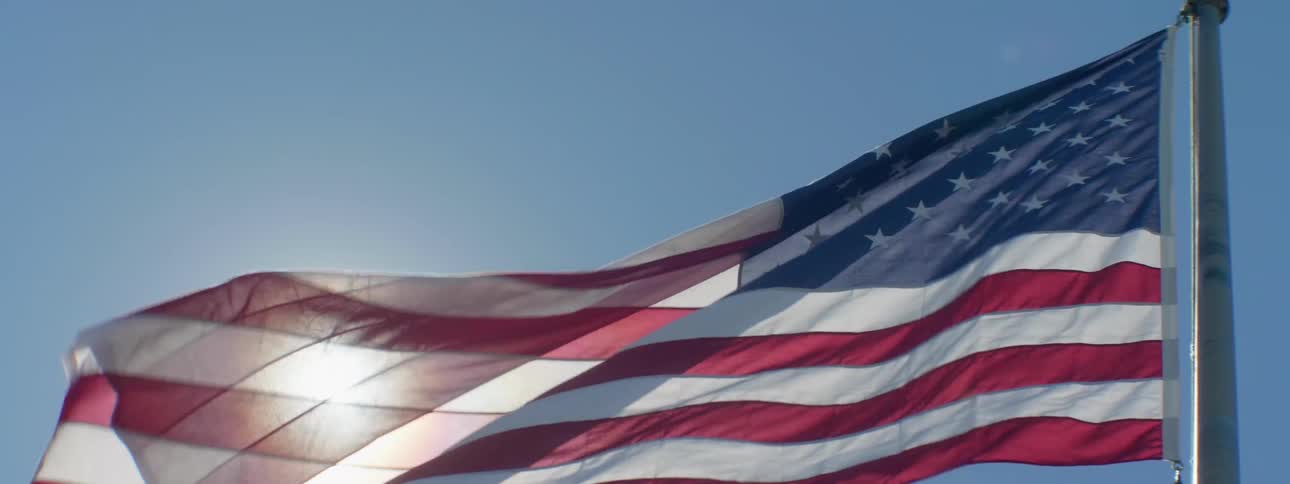 An american flag is swaying and waving in the wind in front of the shining sun