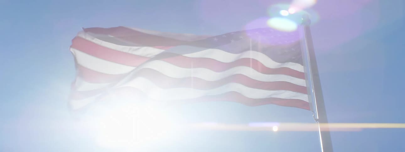 An american flag waves atop a flag pole on a sunny day