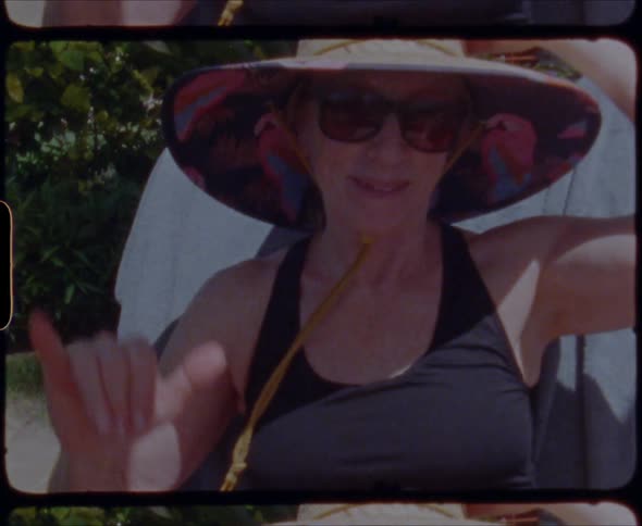 A woman does a shaka wave with her fingers while holding onto her hat
