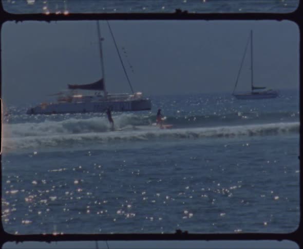 Two surfers ride on wave on surfboards near the boats on sunny day