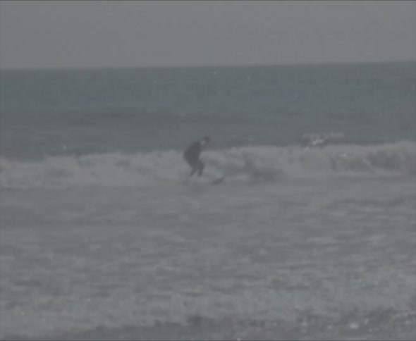 A surfer wearing a black wet suit is riding a big wave