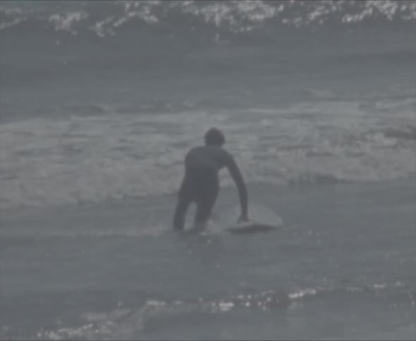 A man walks in to the waves with his surfboard as they crash towards the shore