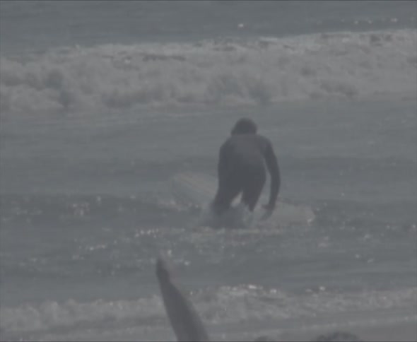 Man with black wetsuit carrying a white surfboard walks into sea