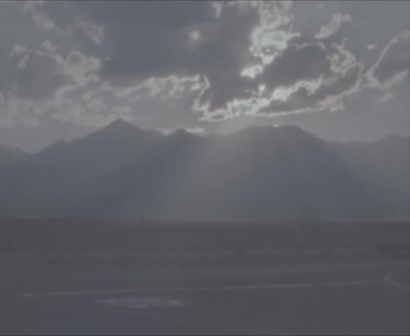 A landscape with a road and vehicle with the sky and clouds in the background