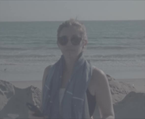 A woman turns around and smiles while standing on the beach with a towel over her shoulders