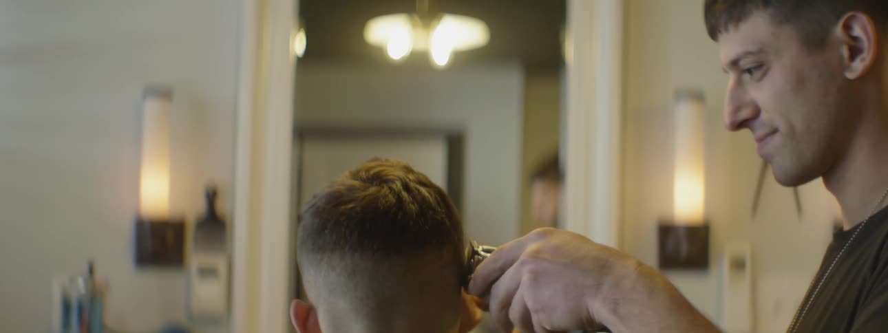 A barber uses an electric razor to cut a man's hair