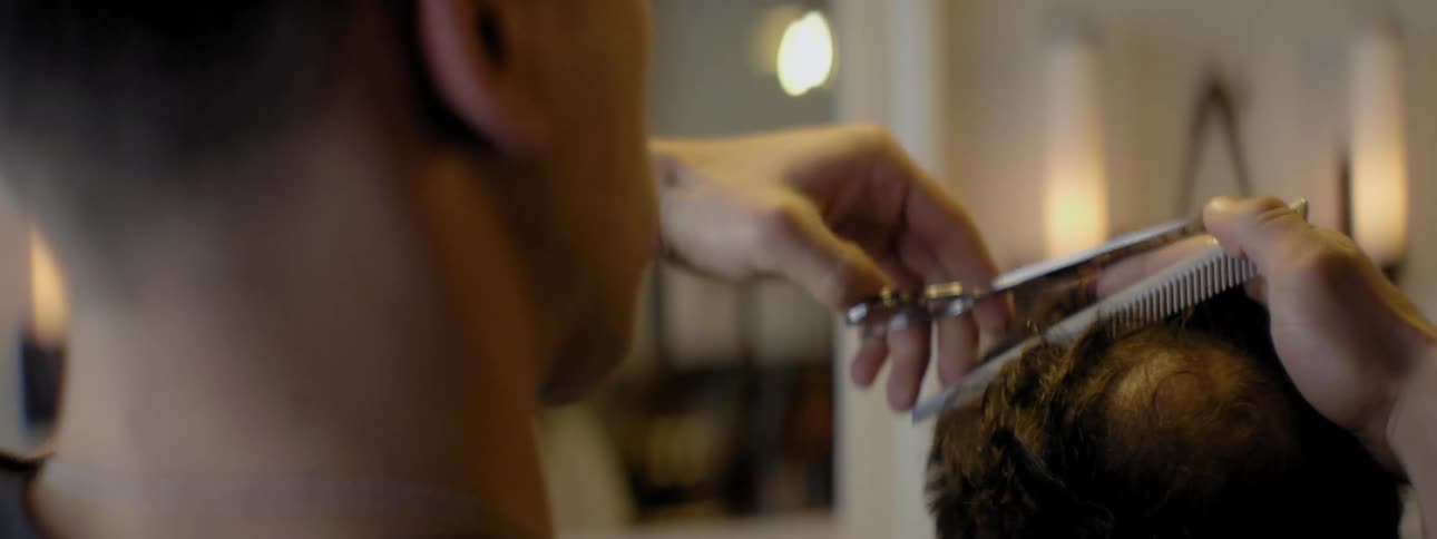 Man uses comb and scissors to cut a person's hair