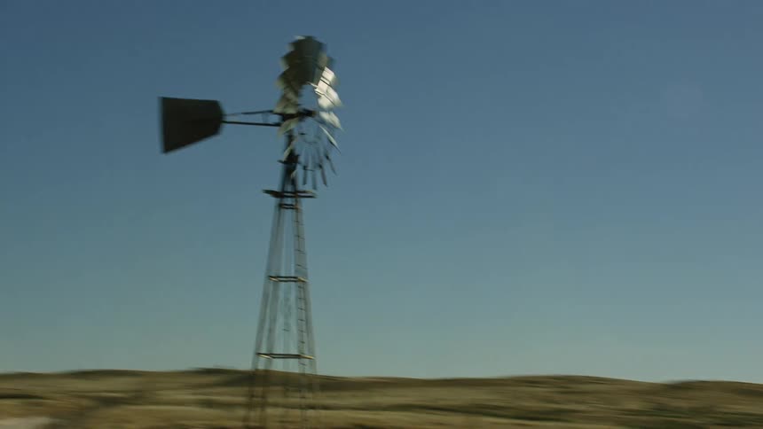Windmill spins over countryside with buildings hills and mountains in background