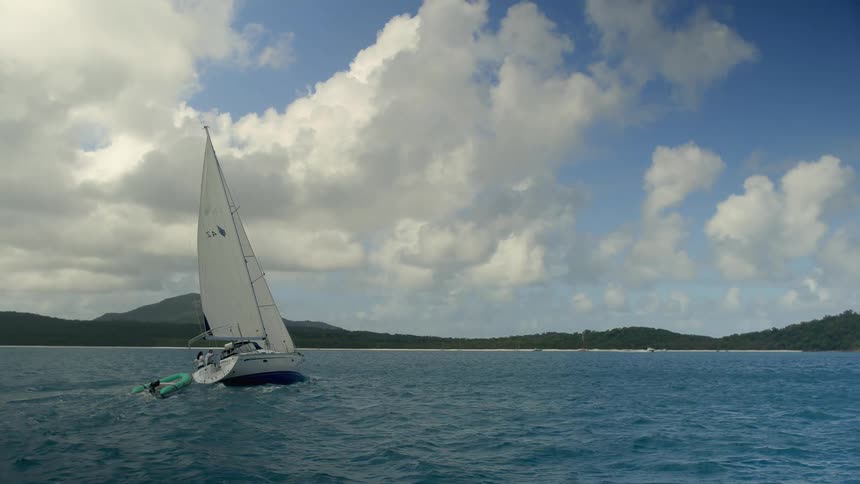 Two people on a sailboat pulling a rubber dinghy