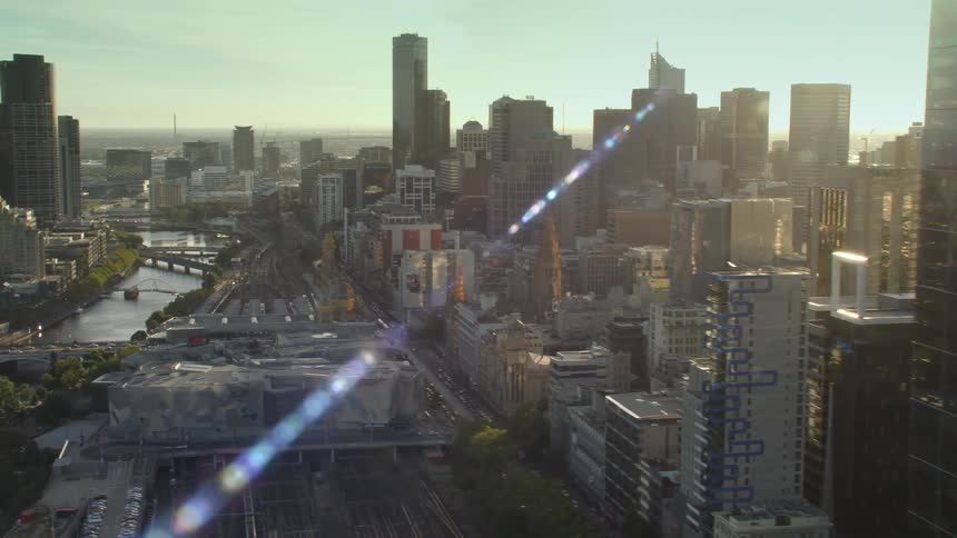 Sun glares across city skyscrapers and bridge crossing river cutting through center of downtown