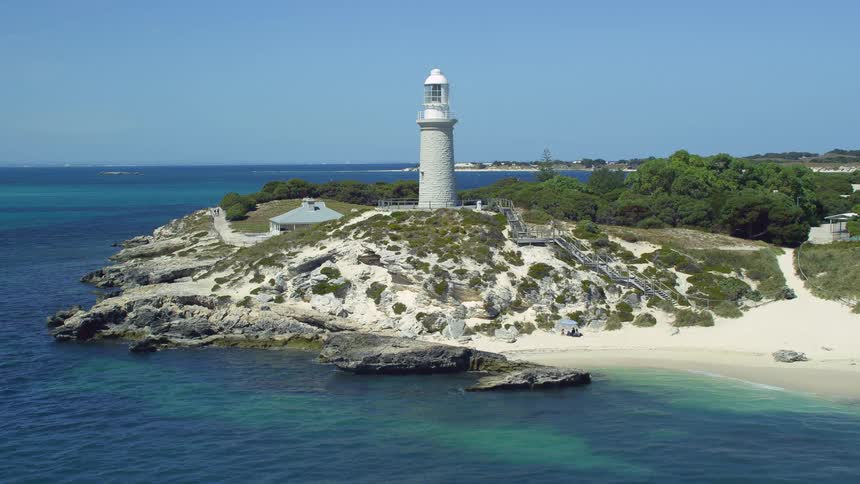 Aerial view of white sand beach with lighthouse on hill next to sea