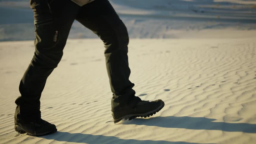 A person walks through the sands of a desert with their hands in their pockets during the day