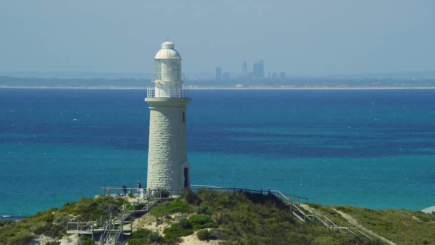 A tall white lighthouse is on top of a hill overlooking the ocean coast