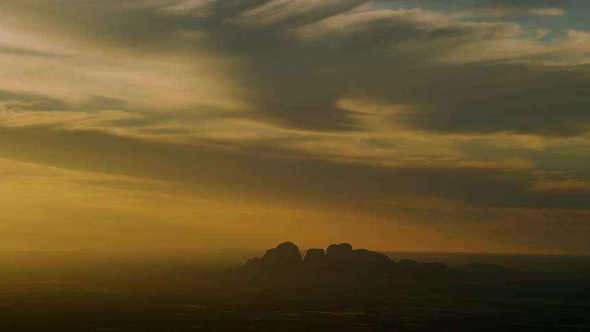 Haze partly obscures rocky mountain under heavily clouded sky