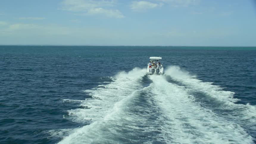 A motor boat leaves a foaming wake as it travels past the coast