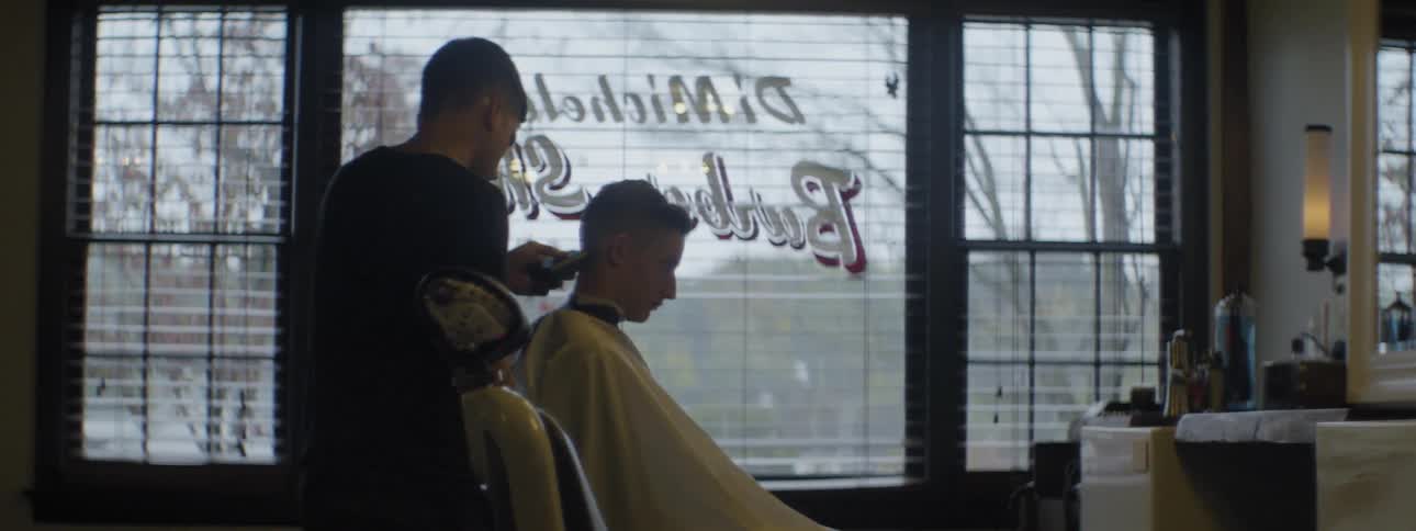 Barber trimming hair off a customer in a yellow cape