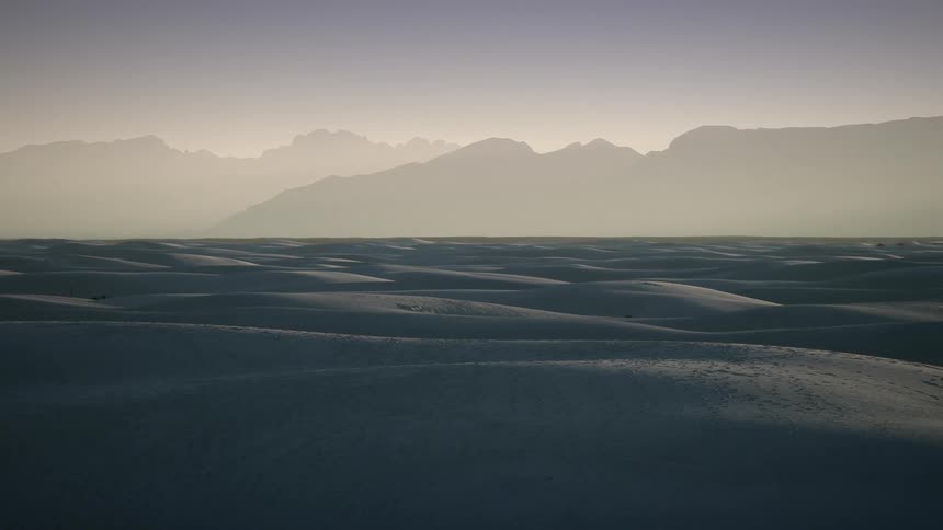 A landscape covered in snow and ice with a mountain range the sky and clouds in the background