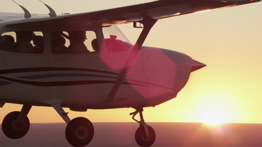 An aerial view alongside a small private plane flying while the sun is setting in the background