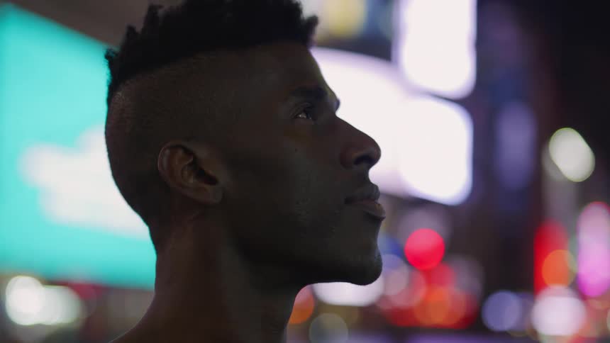 A man is outdoor at night in a city surrounded by lights and staring upwards