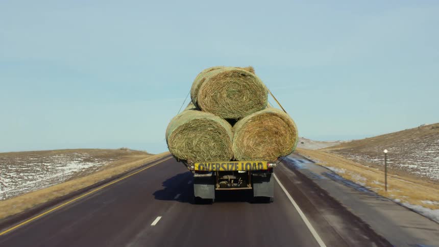 A truck carries oversized bales of hay down a rural highway