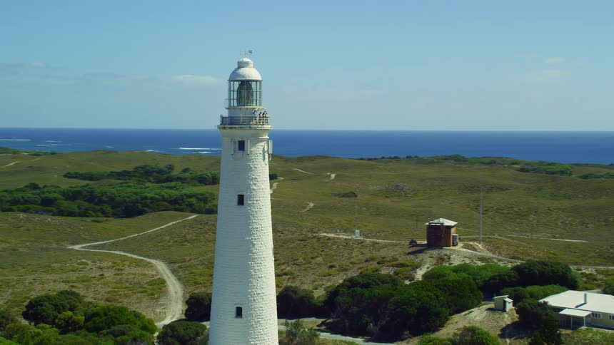 A tall white lighthouse stands on a hill with the ocean and coast behind it