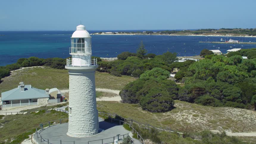A lighthouse on a hill is overlooking the coast and buildings along the shore