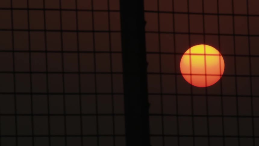 The sky is red as the sun sets behind the fence