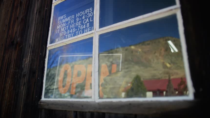 A man flips a sign in the window of a business from closed to open