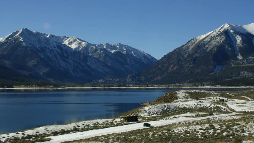 Black car driving on a road near the lake on a landscape covered in snow near the mountain